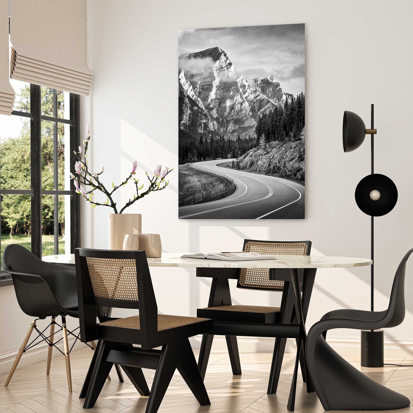 Dining room with a table and chairs, a large mountain landscape painting on the wall, and a modern floor lamp. Winding road through a forest with snow-capped mountains in the background. Kananaskis Country, Fine Art Photography, Dermot O'Kane, Rocky Mountains, Alberta, Canada